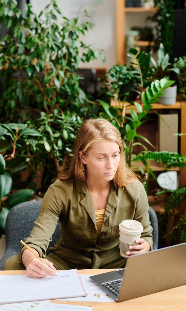 Young creative woman with long blond hair having coffee and making notes